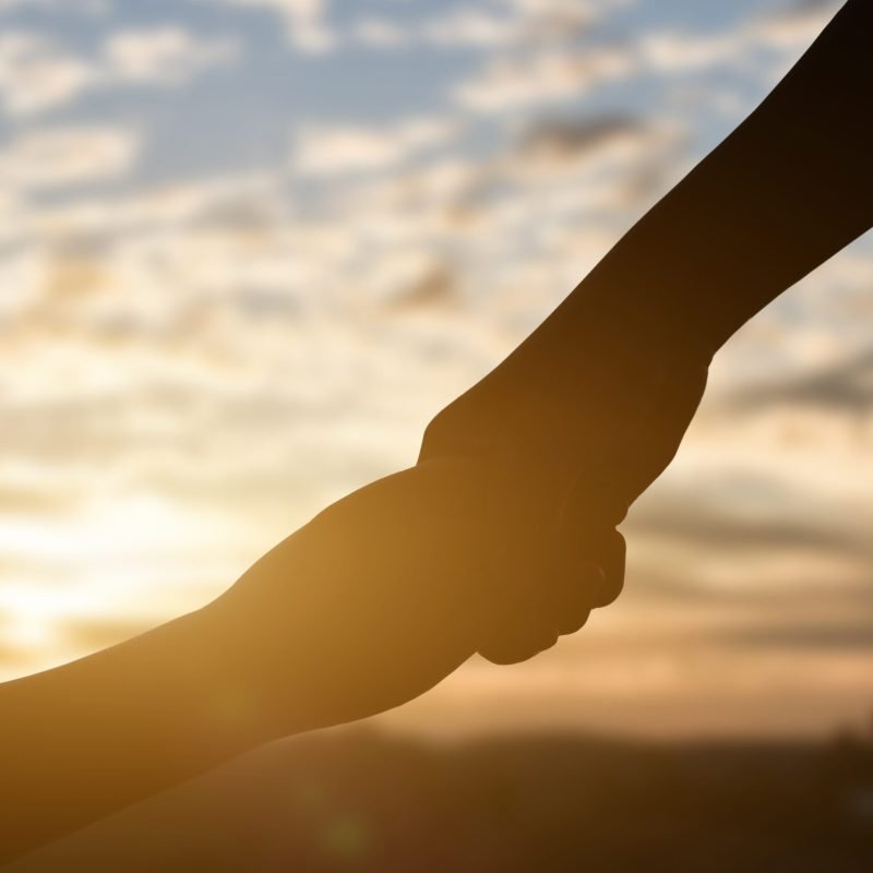 Silhouette of giving a help hand, hope and support each other over sunset background. Concept of helping hands and develop a friendship.